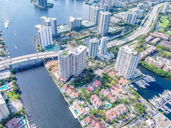 Panoramic aerial view of high-rise buildings near a body of water with a bridge and yachts docked nearby.