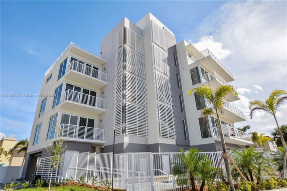 Front view of a modern multi-story building with balconies and a gated entrance.