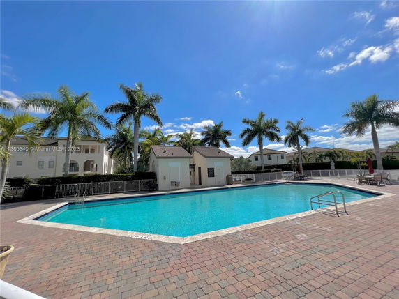 Outdoor swimming pool area with surrounding palm trees and buildings.