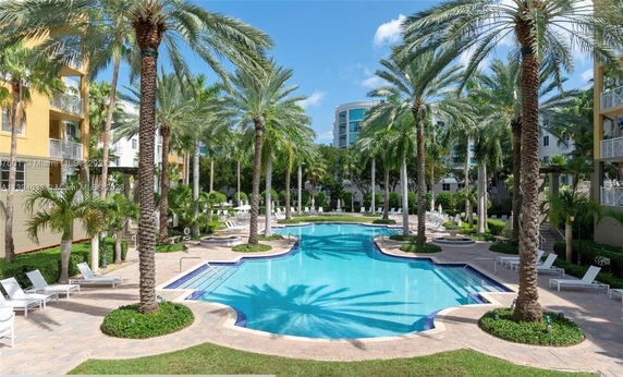 Outdoor swimming pool with surrounding palm trees and lounge chairs in a residential setting.