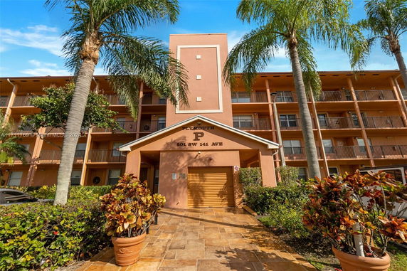 Front view of a multi-story apartment building with balconies and palm trees.