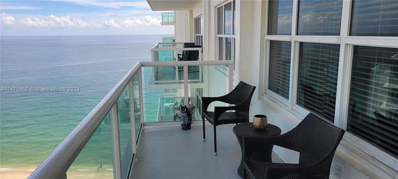 Balcony view of an ocean with clear skies and seating arrangements.