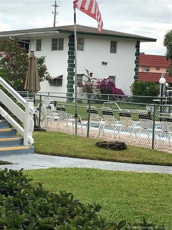 View of an outdoor swimming pool area with surrounding patio chairs and nearby building.