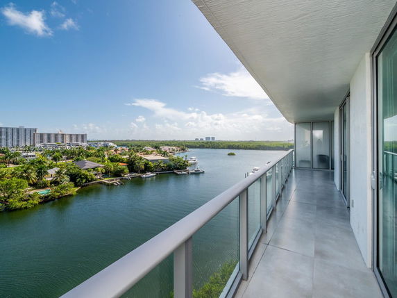 Balcony view overlooking water with buildings and greenery in the distance.