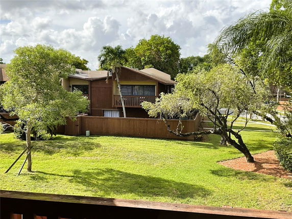 View of a wooden house with a balcony surrounded by trees and grass.