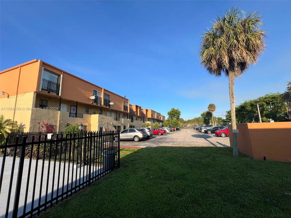 Front view of a multi-story building with balconies and a parking area.