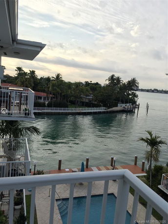 Waterfront view from a balcony overlooking a swimming pool and canal with palm trees.