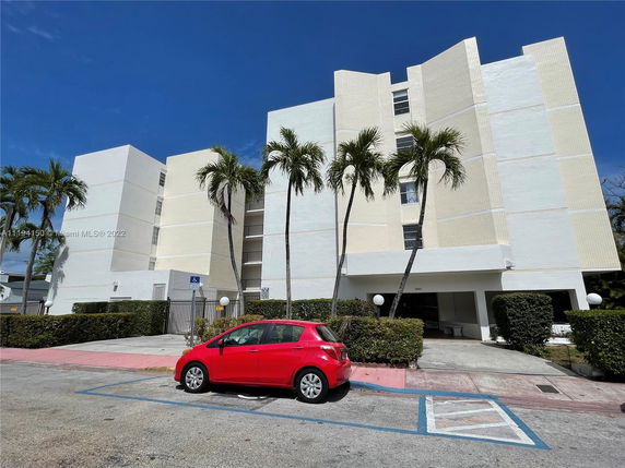 Front view of a multi-story building with a flat roof and a red car parked in front.