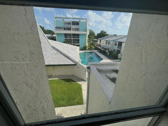 View from a window overlooking a swimming pool and nearby buildings.