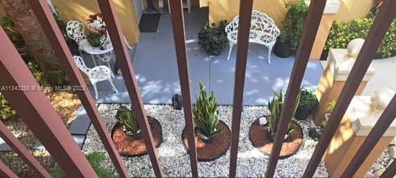 View through a railing of a patio area with chairs and potted plants.