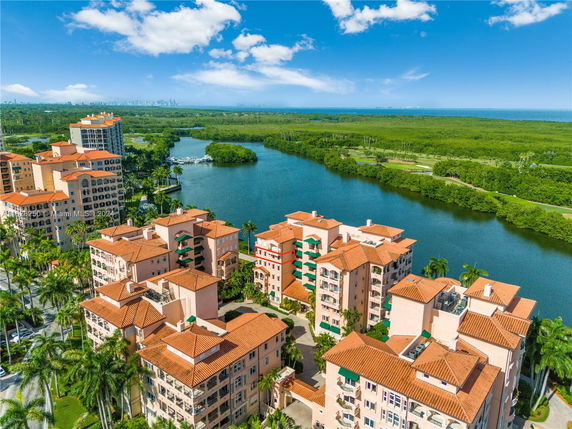 Panoramic view of apartment buildings with terracotta roofs overlooking a body of water and lush greenery.