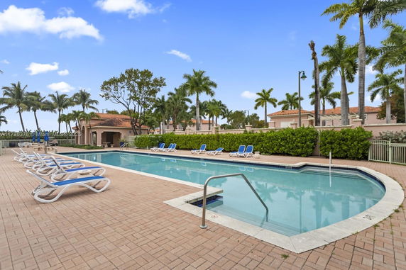 Outdoor swimming pool area with lounge chairs and palm trees.