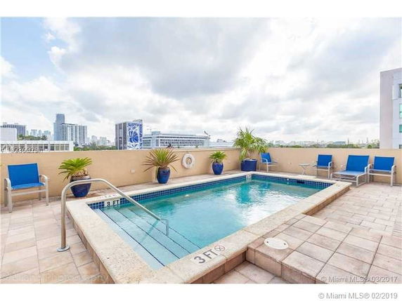 Rooftop with a swimming pool surrounded by blue lounge chairs and potted plants.