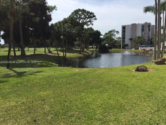 View of a pond and grassy area with trees, adjacent to a multi-story building.