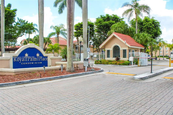 Front view of a condominium entrance with a sign and a small building.