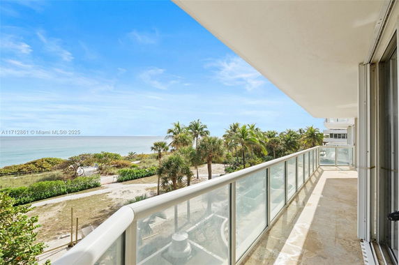 Balcony view overlooking a beach and ocean with palm trees.