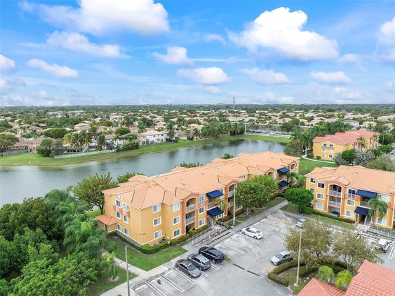 Aerial view showing multiple residential buildings with red roofs near a water body and surrounded by greenery and houses.