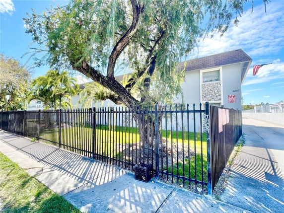 Front view of a building with a black metal fence and a tree in front.