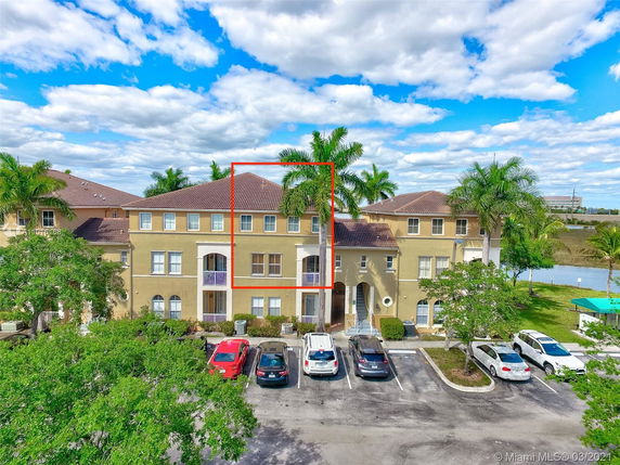 Front view of a multi-story residential building with parking area in front.