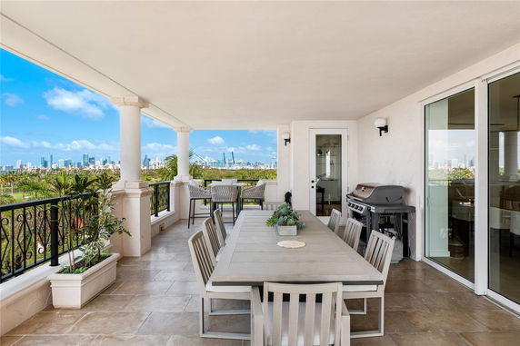 Covered outdoor dining area with a table, chairs, and a barbecue grill, offering a panoramic view of the city skyline.