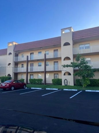 Front view of a multi-story building with balconies and parking area.