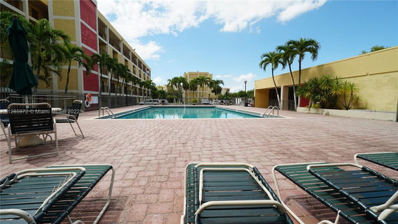 Outdoor swimming pool area with lounge chairs and surrounding multi-story buildings.