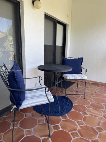 Outdoor seating area on a terracotta-tiled patio with two chairs and a round table.