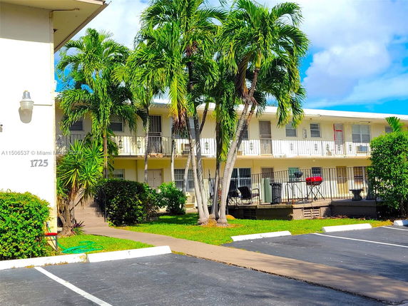 Front view of a two-story residential building with balconies and palm trees.