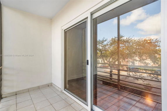 Balcony area with sliding glass door overlooking trees and parked cars.