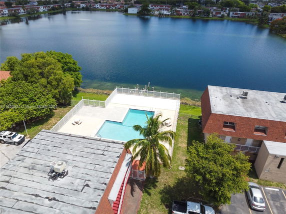 Aerial view of a residential area by a lake, showing a swimming pool and buildings.