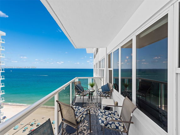 Balcony view overlooking the ocean with chairs and a table.
