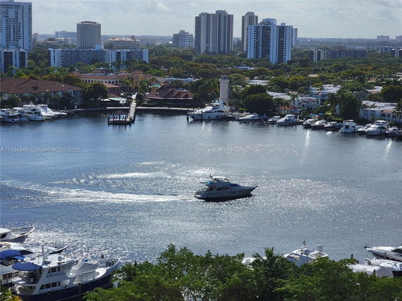 View of a marina with several boats docked, surrounded by residential buildings and high-rises in the background.