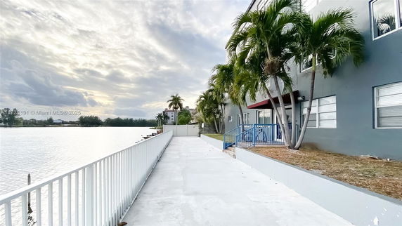 View of a multi-story building with palm trees along a waterside pathway.