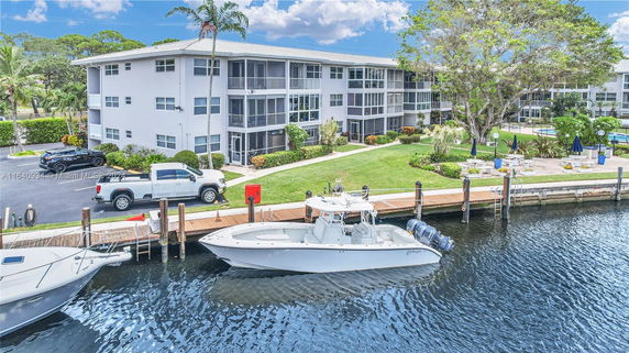 View of a waterfront residential building with multiple floors and surrounding greenery.