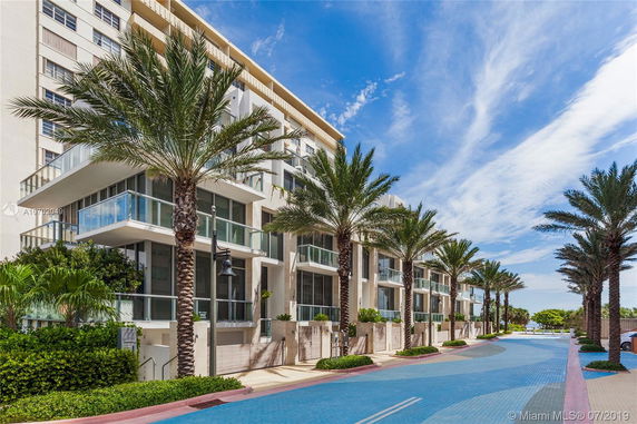 Front view of a multi-story building with glass balconies and palm trees.