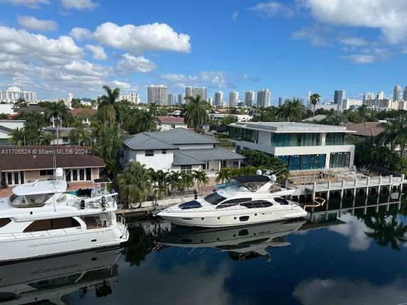 View from a waterway showing houses with yachts docked near them and a cityscape in the background.