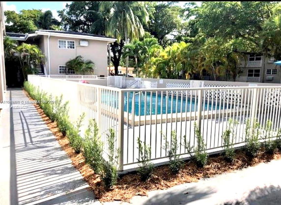 Outdoor swimming pool area surrounded by a fence, with a residential building in the background.