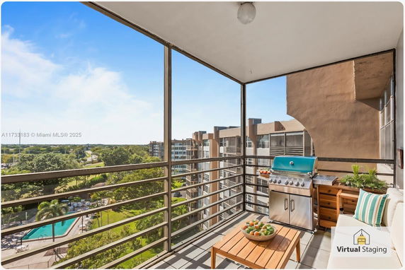 Balcony view of a high-rise building with outdoor furniture and a grill, overlooking surrounding residential buildings and greenery.
