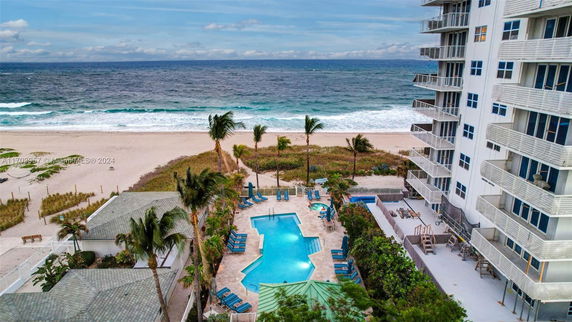 Outdoor swimming pool area with beach and ocean view next to a multi-story building.