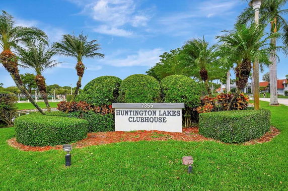 Sign for Huntington Lakes Clubhouse surrounded by landscaped greenery and palm trees.