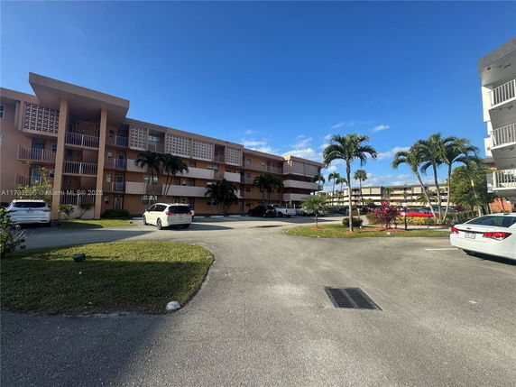 Front view of a multi-story apartment building with balconies and parking area.