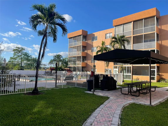 Front view of a multi-story building with a fenced swimming pool and outdoor seating area.