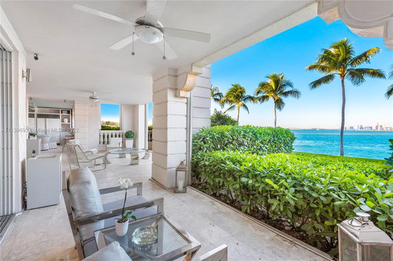 Panoramic view of a patio area with outdoor furniture, ceiling fans, and a view of the ocean and palm trees in the background.