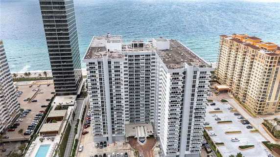 Aerial view of a high-rise building near the ocean with other buildings nearby.