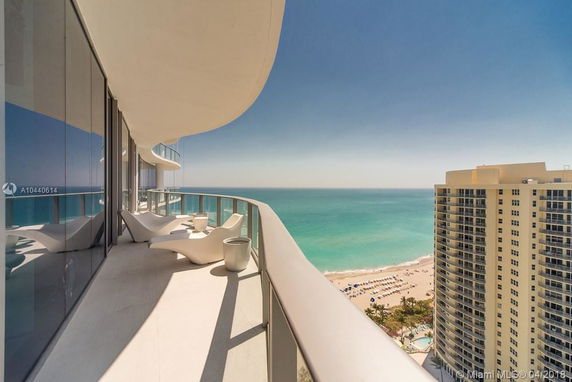 Panoramic view from a high-rise balcony overlooking the ocean and nearby buildings.