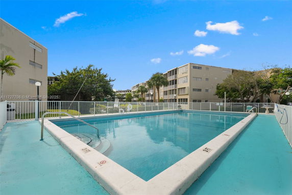 Outdoor swimming pool with a fenced perimeter and adjacent buildings.