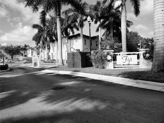 Front view of a residential complex gated entrance with palm trees and signage.