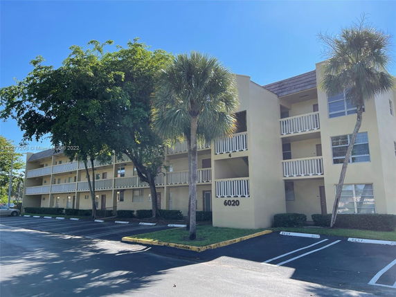 Front view of a three-story apartment building with balconies and parking spaces in front.