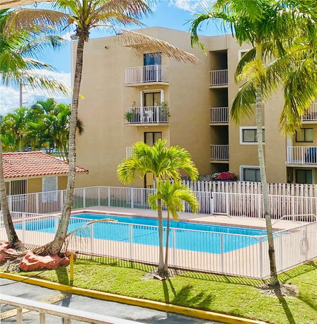 Outdoor swimming pool surrounded by a fence next to a multi-story building with balconies.
