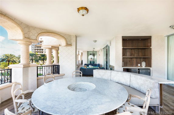 Outdoor patio area with round marble table and cushioned seating, featuring arched columns and a view of nearby buildings.